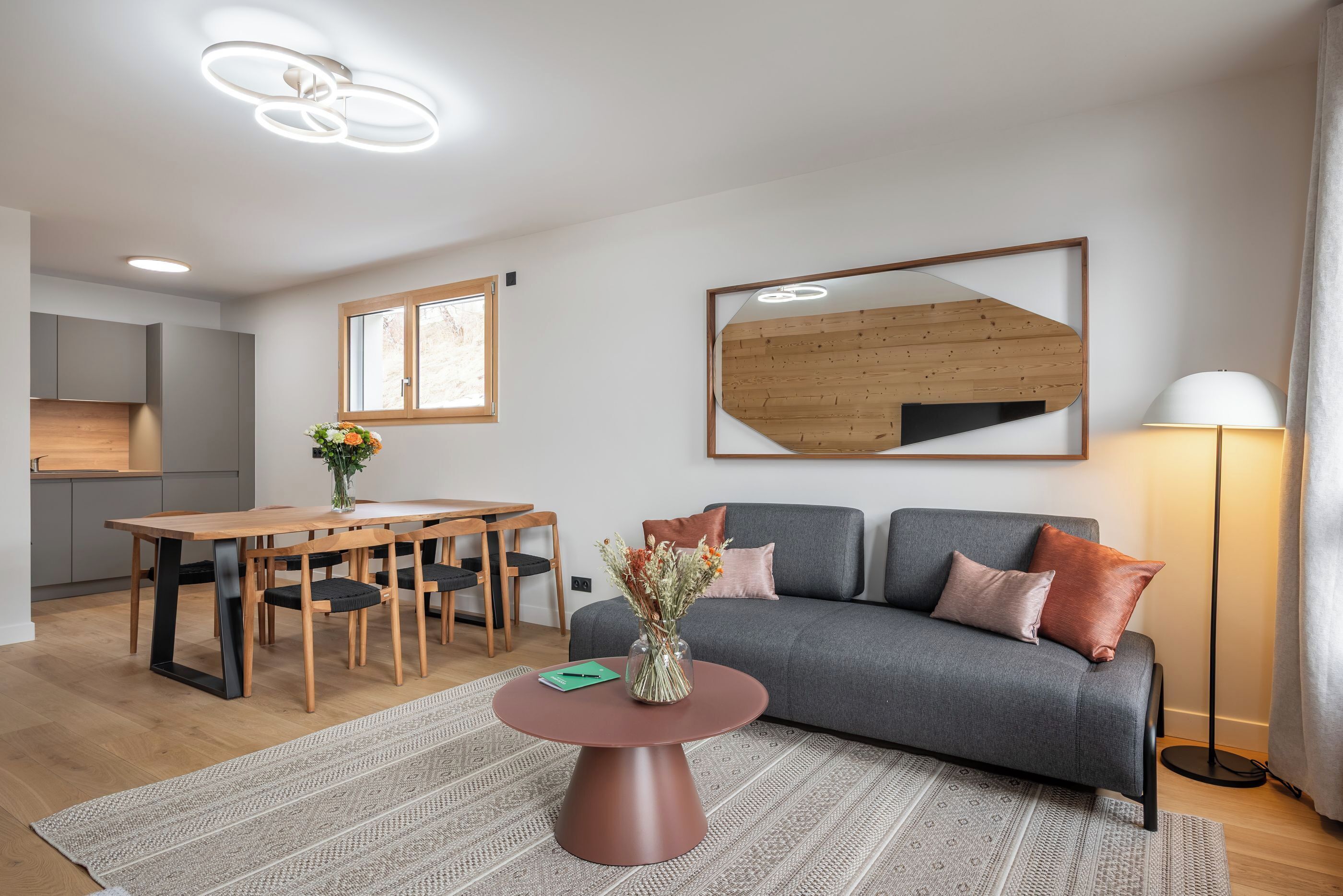 Un salon moderne avec un canapé gris, une table à manger en bois et une table basse sur laquelle est posé un vase.