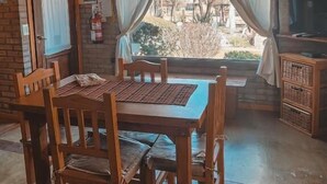 Une table à manger en bois avec des chaises, un mur en briques, une fenêtre avec des rideaux et un téléviseur posé sur un meuble en bois.