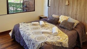 Une chambre avec un grand lit, un plancher en bois, une fenêtre donnant sur un paysage verdoyant et une tête de lit en bois.