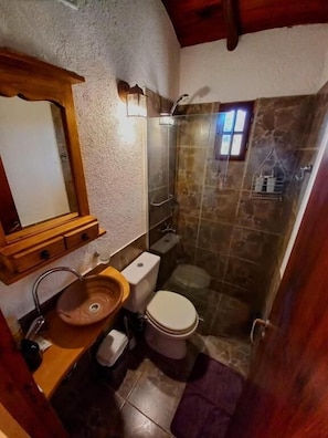 Un baño pequeño con tocador de madera, inodoro, cabina de ducha y un ventanal.