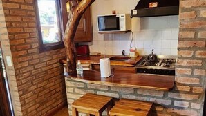 Une cuisine avec un mur en briques au style rustique, des tabourets de bar en bois, un four à micro-ondes et une cuisinière à gaz.