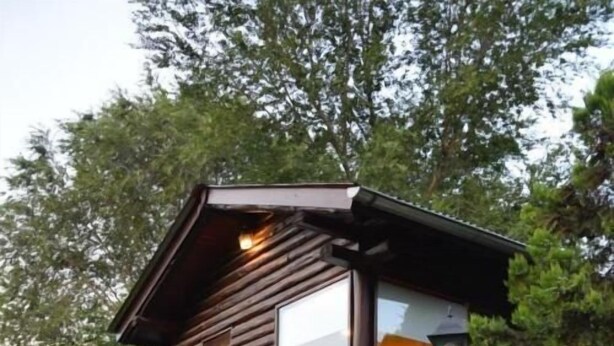 Une cabane en rondins dotée d’une grande fenêtre, d’un porche et d’un lampadaire.