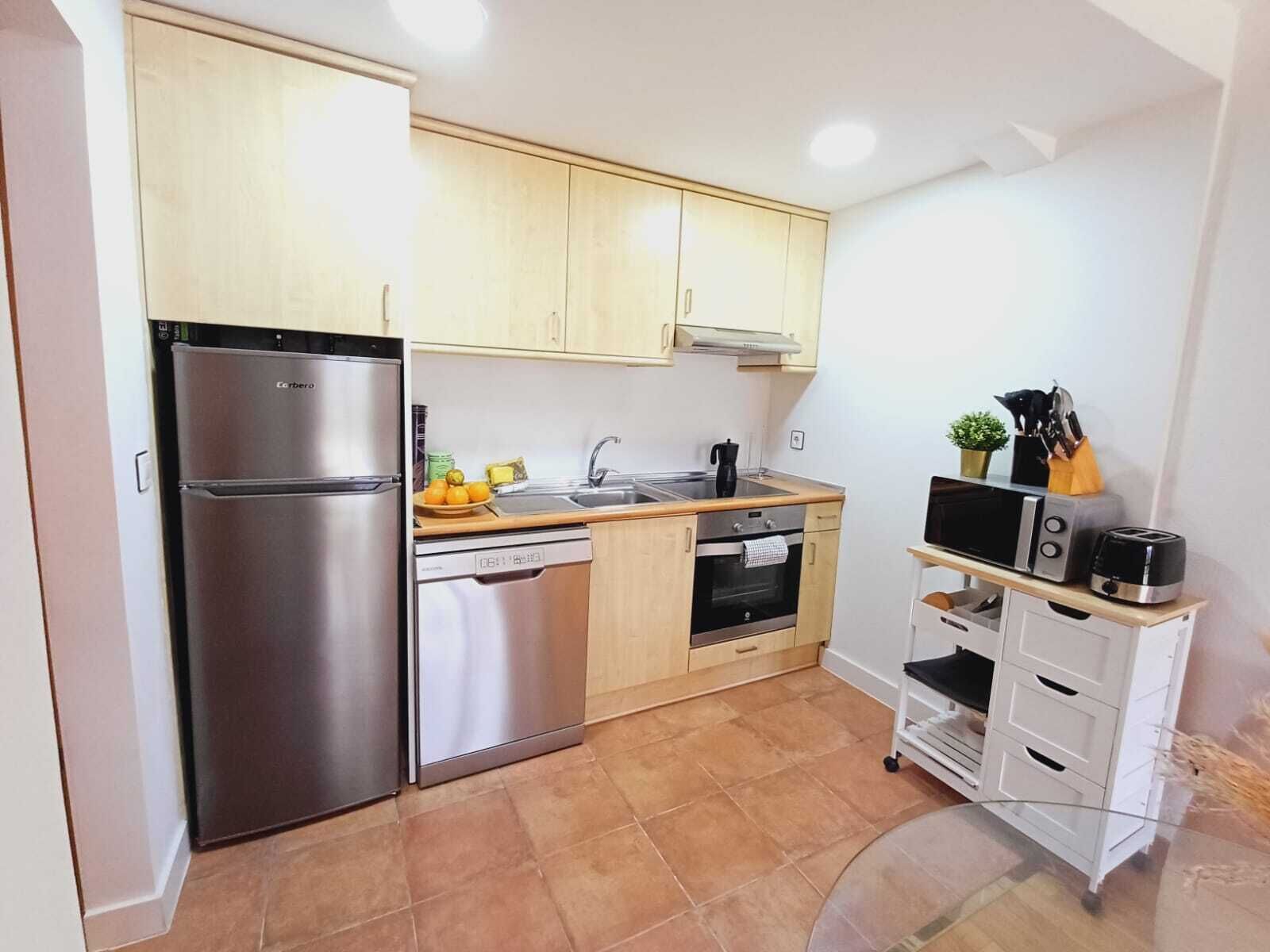 Una cocina compacta con refrigerador de acero inoxidable, lavavajillas, estufa y microondas.