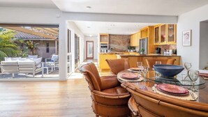 Una cocina moderna con armarios de madera, un comedor con mesa de vidrio y un patio con mobiliario exterior.