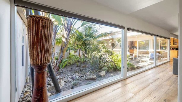 Un interior moderno con grandes puertas correderas de vidrio que dan a un jardín con plantas tropicales y piso de madera.