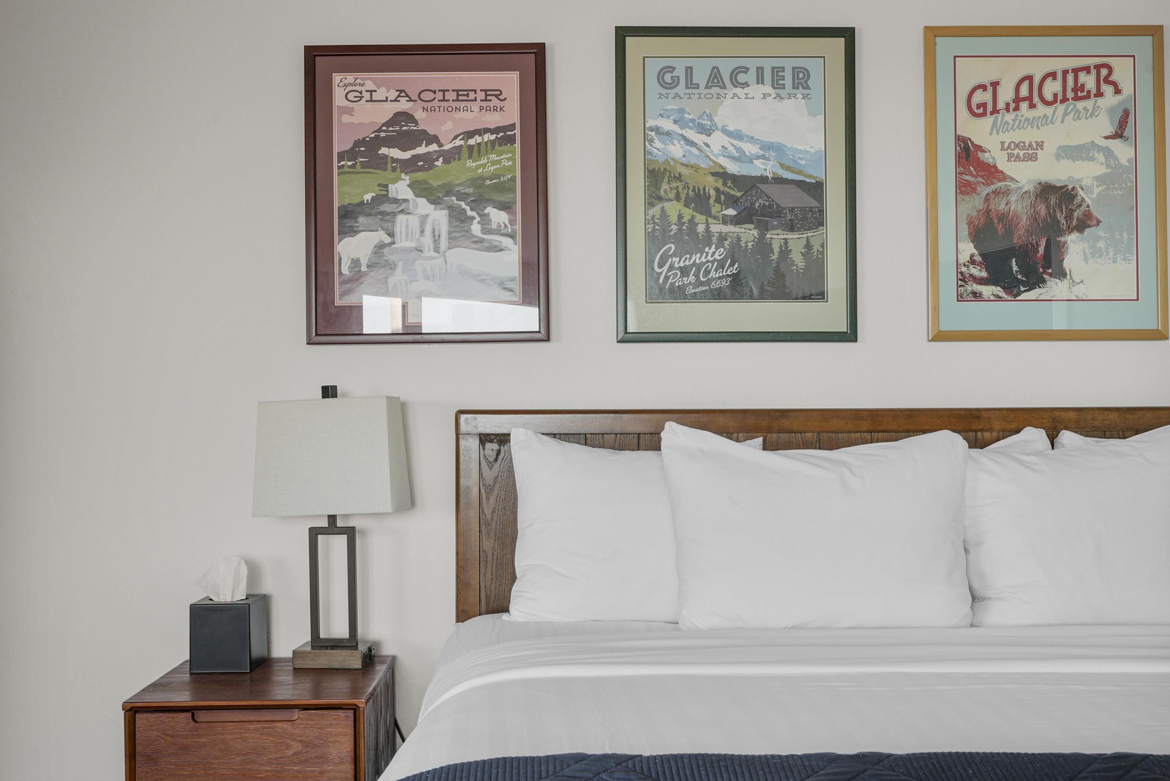 A hotel room with a bed, a nightstand with a lamp, and three framed posters on the wall.