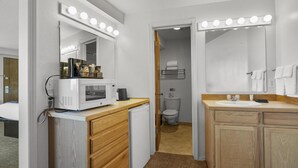 Et lille badeværelse med et håndvaskeskab, en mikroovn og et toilet, der kan ses gennem en åben dør.