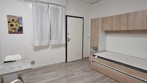 A room with a white door, a small table with chairs, a bed with wooden headboard, and a painting on the wall. - Independent Room with Private Access in Fairgrounds (Bologna)