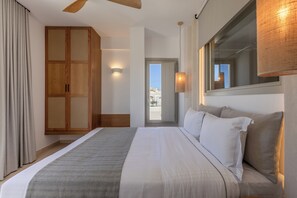 A bedroom with a bed, a wardrobe, a window, and a door leading outside. - Evira Suites (Santorini)