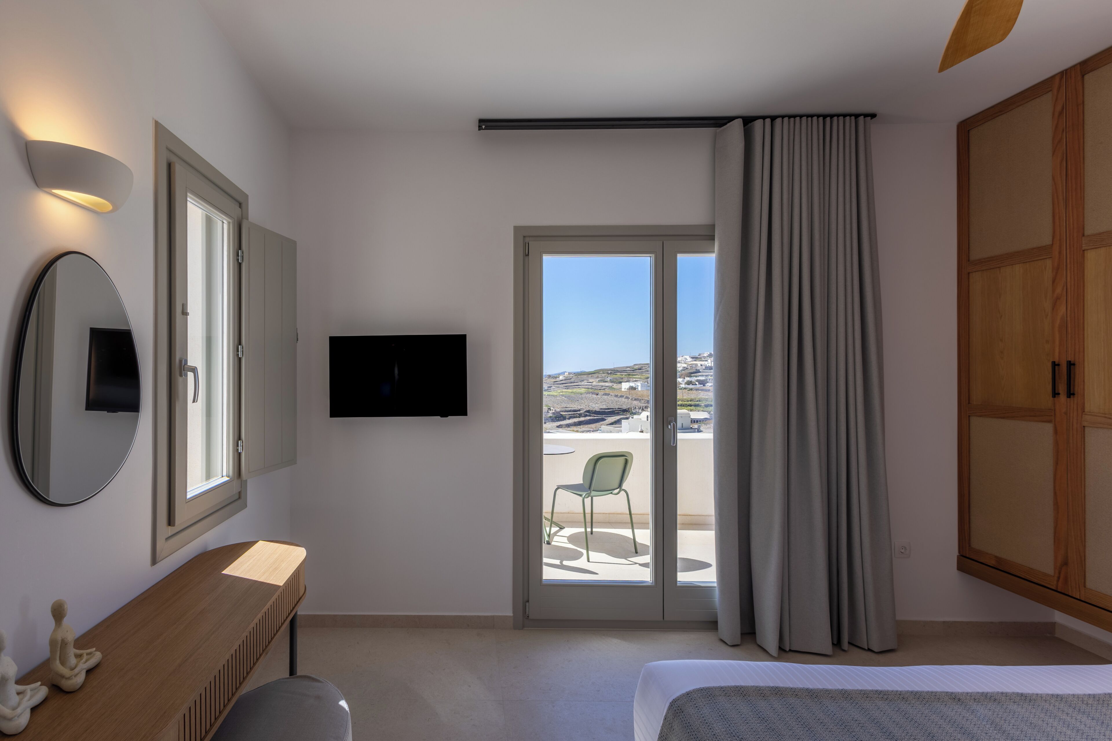 Ein Hotelzimmer mit einem Bett, einem Schreibtisch, einem Stuhl, einem Fernseher und einer Glastür zu einem Außenbereich.