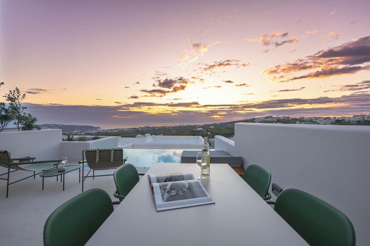 A rooftop terrace with a table, chairs, a magazine, and a bottle of wine.