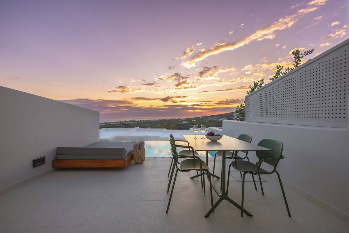 A terrace with a table and chairs, a pool, and a sunset view.