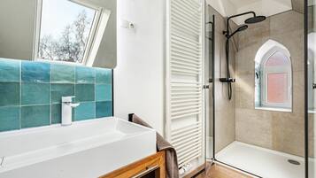 A bathroom with a white sink, a shower with a glass door, and a window with a view of trees.
