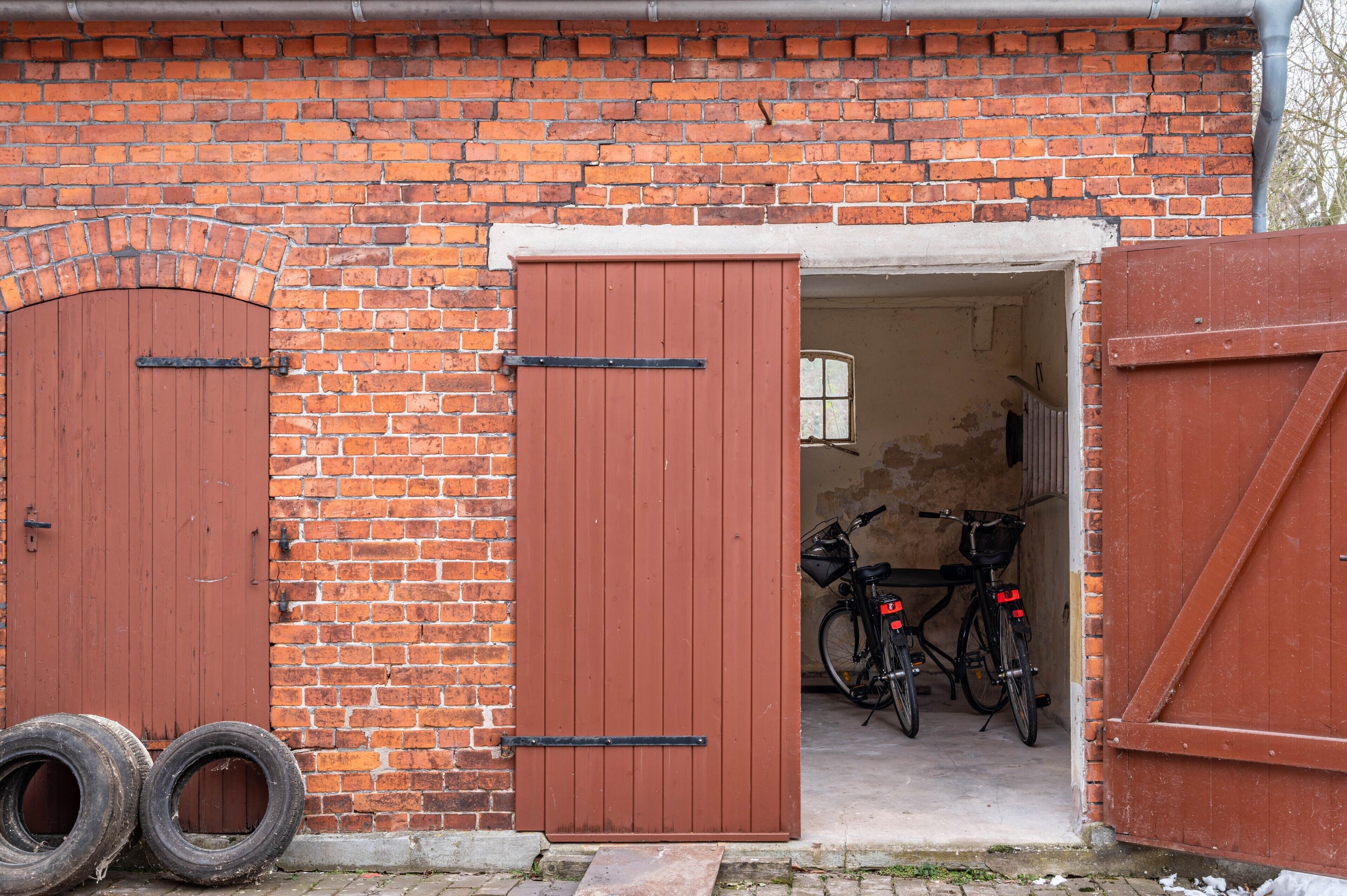 A brick building with two wooden doors, a bicycle, and two tires outside.