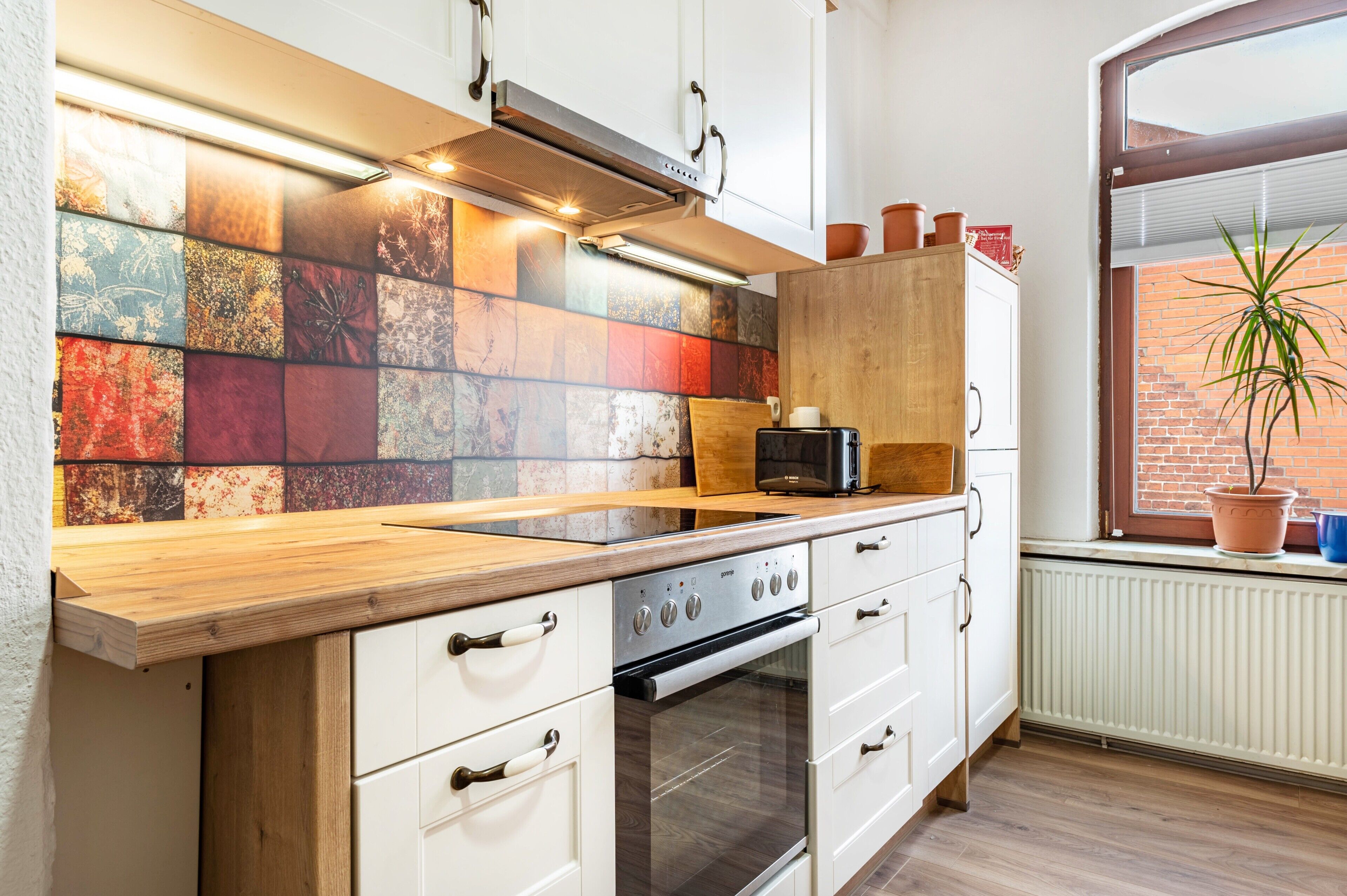 Une cuisine dotée d’un plan de travail en bois, de meubles blancs, d’un pare-feu en carrelage et d’une fenêtre donnant sur un bâtiment en briques.