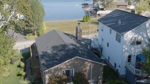 A residential area with a large white house, a smaller attached building, and a body of water in the background.