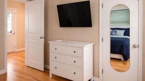 A bedroom with a wooden floor, a white dresser, a flat-screen TV, and a door with a mirror.