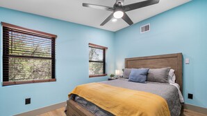 Camera da letto con un letto, due finestre, una ventola a soffitto e un comodino con una lampada.