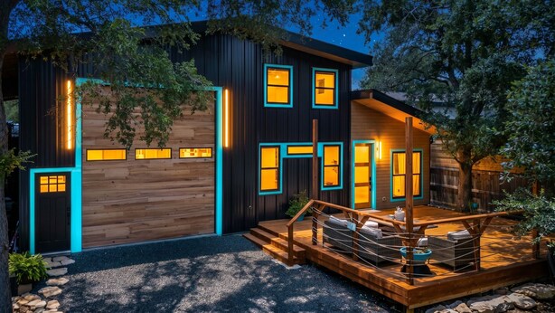 Una casa moderna con facciata in legno, diverse finestre e una terrazza con mobili da esterno.