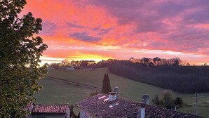 Ein ländliches Haus mit Ziegeldach, ein Auto davor geparkt, und Blick auf den Sonnenuntergang über einem Feld.