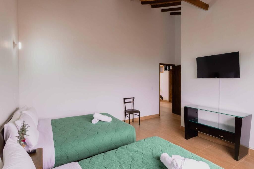 Una habitación con dos camas, una silla, un televisor y un mueble de vidrio para la televisión.