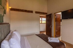 Habitación de hotel con cama, televisión montada en la pared y puerta que da a otra habitación.