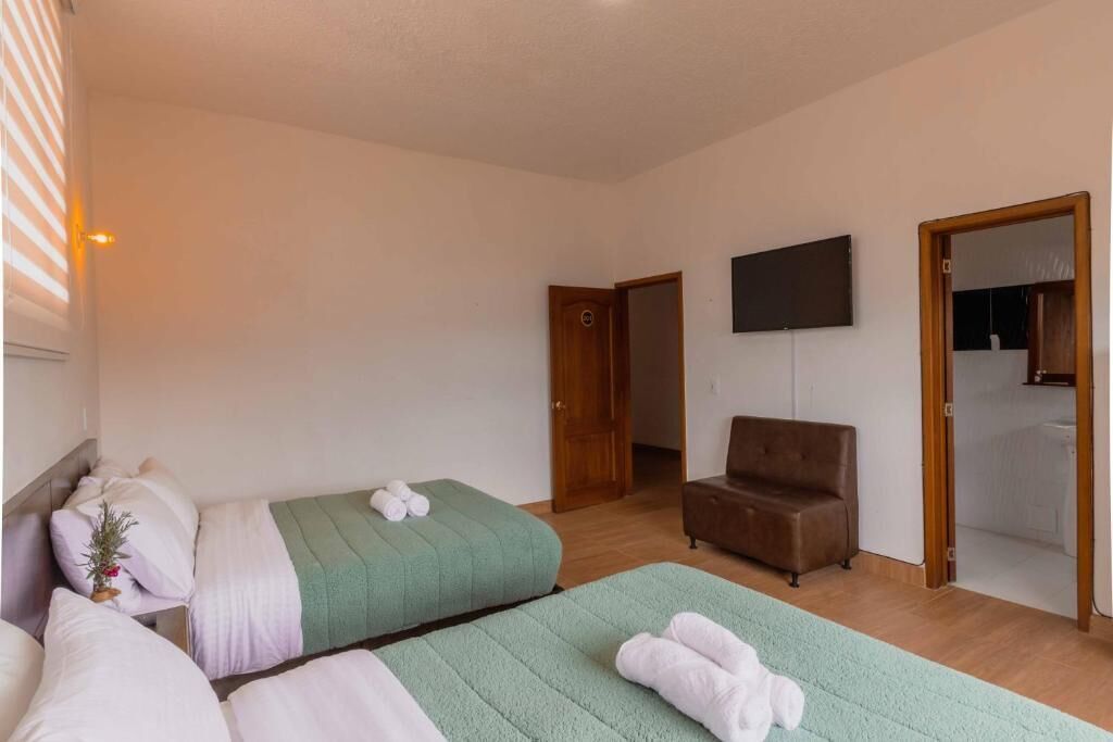 Hotellihuoneessa on kaksi sänkyä, ruskea nojatuoli, televisio ja kylpyhuone, joka näkyy avoimesta ovesta.