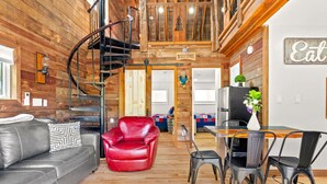 A modern interior with a wooden staircase, a red leather chair, a dining area with a table and chairs, and a kitchen area. - Barn-Again. Private Lake, Mtn view, fishing (Big Indian)