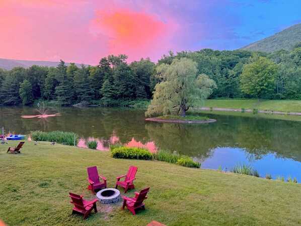 A lakeside view with a grassy area, a fire pit, and red chairs.