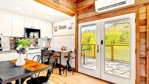 A modern kitchen with white cabinets, a dining area with a wooden table and chairs, and a view of a green landscape through a glass door. - Barn-Again. Private Lake, Mtn view, fishing (Big Indian)
