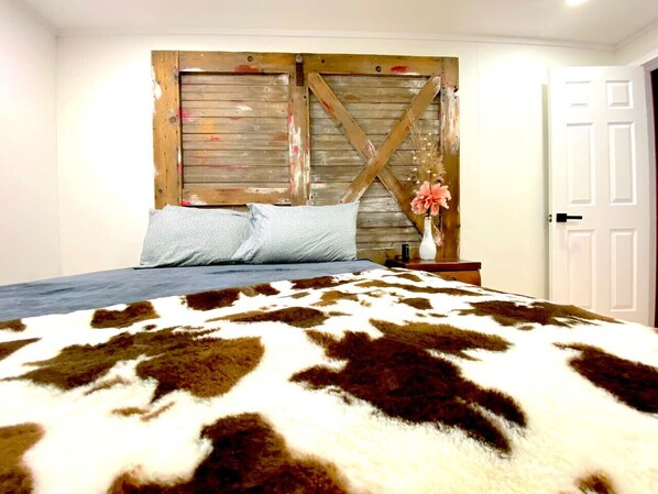 A bedroom with a bed, a wooden headboard, a white door, and a floral arrangement on the nightstand.