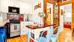 A kitchen with white cabinets, a stove, and a coffee machine. There is a wooden island with chairs and a vase of flowers.