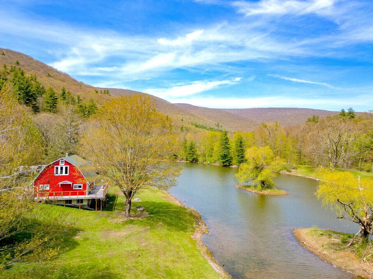 Un granero rojo con porche, rodeado por un río y un paisaje verde.
