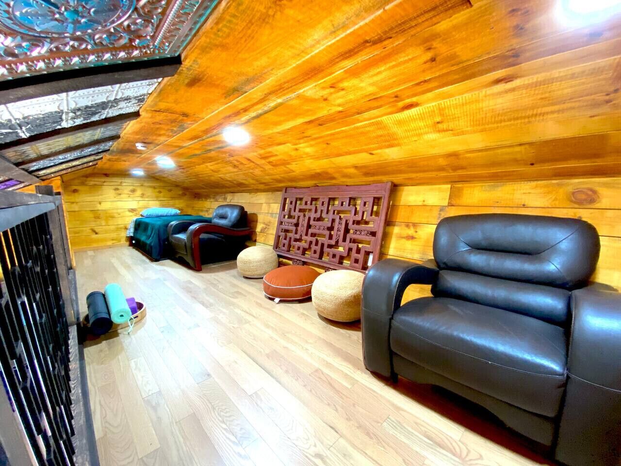 A wooden interior with a black leather sofa, a patterned wall decoration, and a small seating area with cushions.