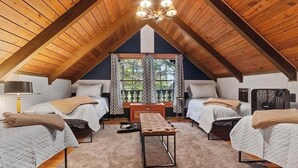 Ein gemütliches Schlafzimmer im Dachgeschoss mit zwei Betten, einer Bank und einem großen Fenster mit Vorhängen.