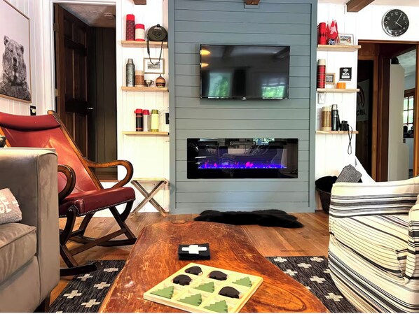 Una sala de estar con televisor, chimenea, sillón de cuero rojo y una mesa de centro con un juego.