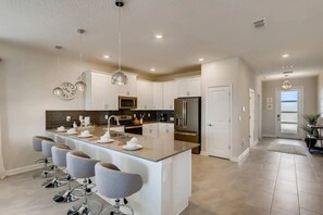 A modern kitchen with a central island, stainless steel appliances, and a dining area with bar stools. - 9BR Vacation Home Near Disney | Sleeps 24 (Kissimmee)