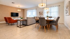 A modern living room with a sofa, dining table, chairs, and a TV. - 9BR Vacation Home Near Disney | Sleeps 24 (Kissimmee)