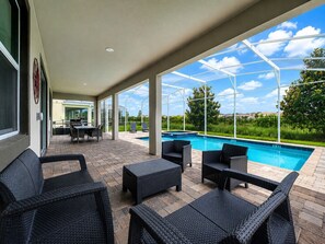 A covered outdoor area with a pool, wicker furniture, and a view of the landscape. - 9BR Vacation Home Near Disney | Sleeps 24 (Kissimmee)