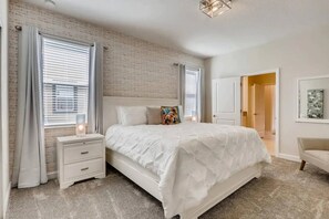 A bedroom with a large bed, a nightstand, a bedside table, and a door leading to another room. - 9BR Vacation Home Near Disney | Sleeps 24 (Kissimmee)