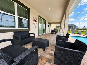 An outdoor patio with wicker furniture, a pool, and a clear view of the sky. - 9BR Vacation Home Near Disney | Sleeps 24 (Kissimmee)
