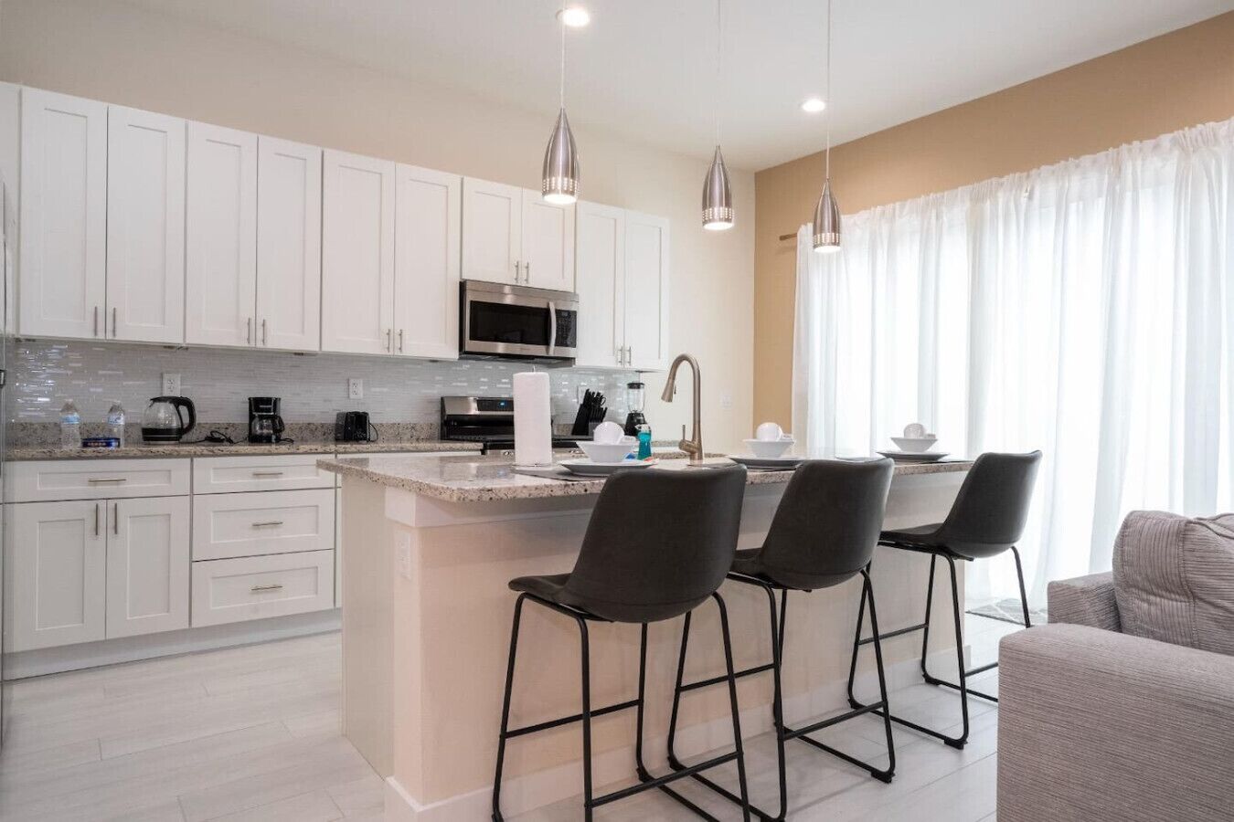 A modern kitchen with white cabinets, a central island with bar stools, stainless steel appliances, and pendant lighting.