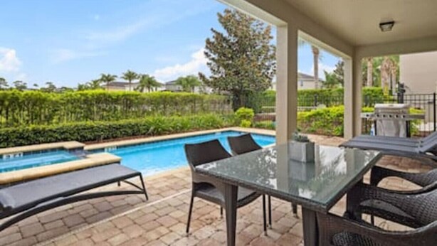 A covered outdoor area with a pool, lounge chairs, and a table. - 381 Fantastic Home Near Disney 5BD/5BT/14P (Kissimmee)