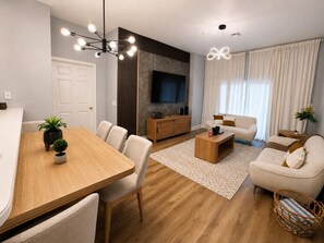 Ein modernes Wohnzimmer mit einem Holzesstisch, einer Couch, einem Couchtisch und einem an der Wand montierten Fernseher.