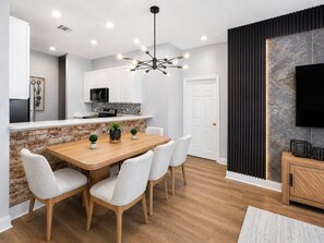 A modern kitchen with white cabinets, a wooden dining table, and a black ceiling light fixture. - Best Value! 3BR Near Disney – Sleeps 8 (Davenport)