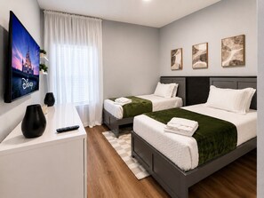 Ein Hotelzimmer mit zwei Betten, einem Fernseher, einem Schreibtisch und einem fensterbepflanzten Fenster.