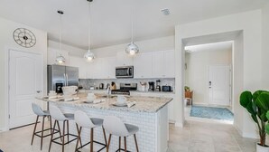 Une cuisine moderne dotée d’un îlot central, de tabourets de bar, d’appareils électroménagers en acier inoxydable et de luminaires suspendus.