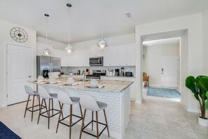 A modern kitchen with a central island, bar stools, stainless steel appliances, and pendant lighting. - Family Paradise | 5BR in Solterra | Close Disney (Davenport)