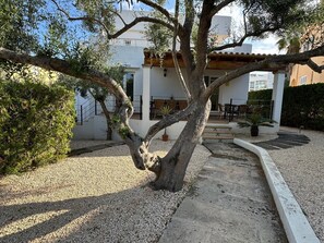 Ein Innenhof mit Baum, Kiesweg und einem Gebäude mit Außenbestuhlung.
