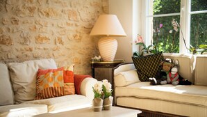 A cozy living room with a stone wall, a lamp, a sofa, and a window with plants.